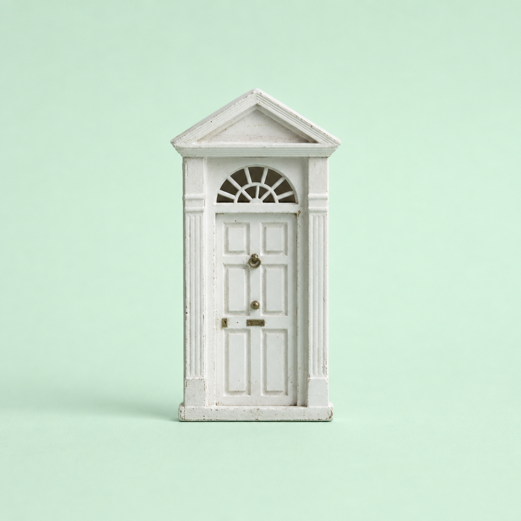 A miniature white front door with classical columns and a fanlight window stands upright against a pale green background, symbolizing Philippine real estate talk and issues like buyer trust, flood risk, legal transparency, and infrastructure.